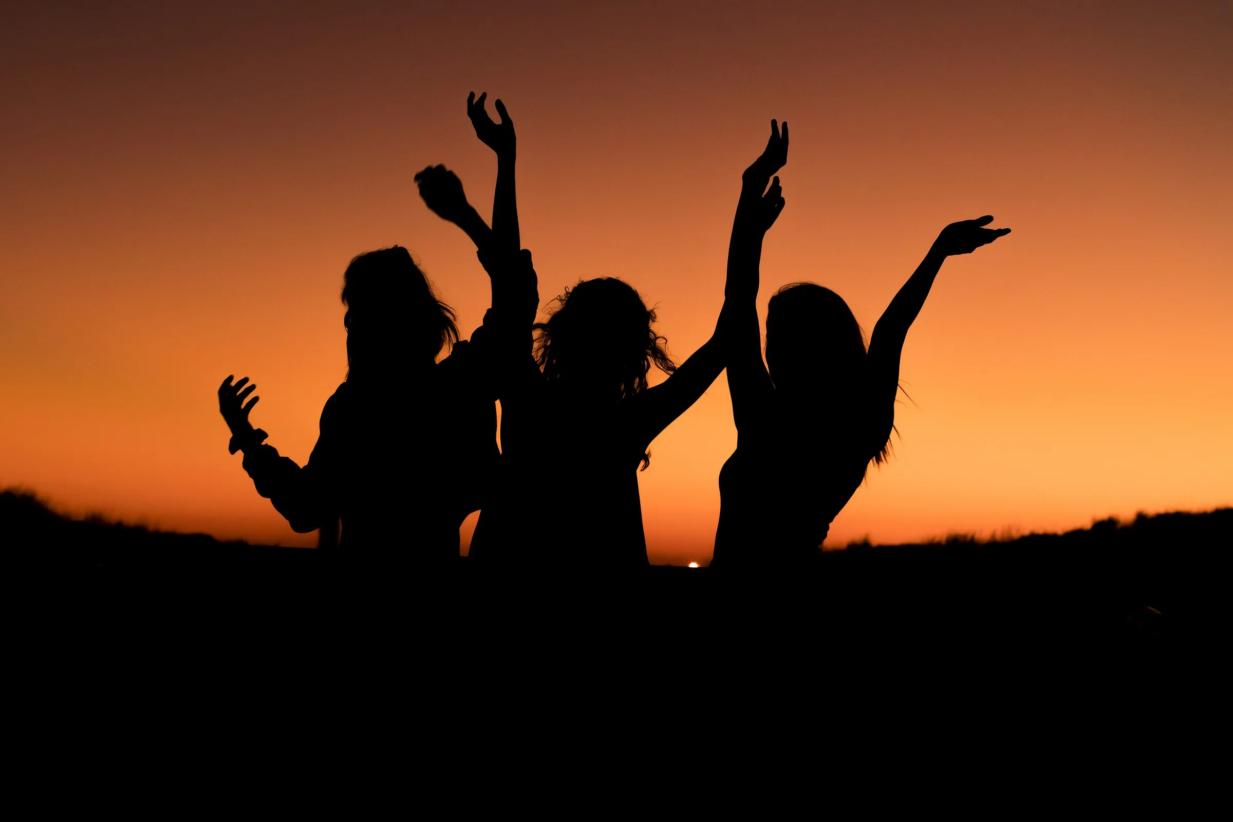 Drei Personen stehen bei Sonnenuntergang auf einem Gipfel